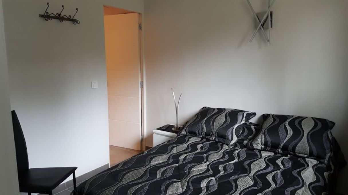 A bedroom with a bed, a chair, a nightstand, and a wall-mounted light fixture.