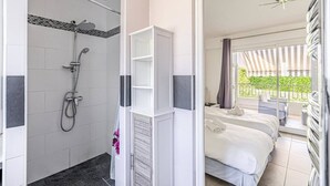 Une chambre d’hôtel avec douche, un lit, un balcon avec vue et un petit coin salon.
