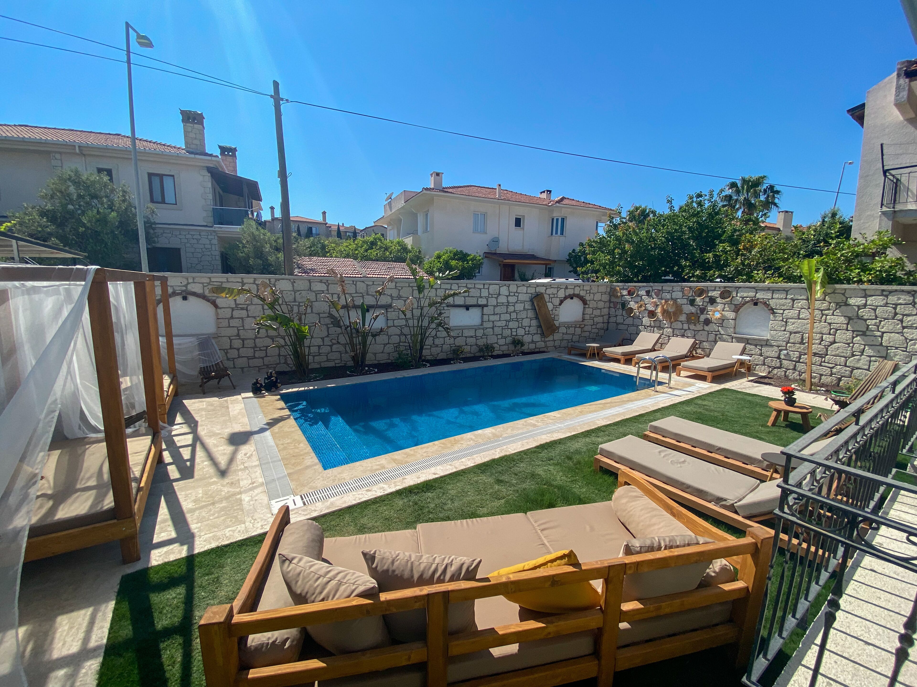 A backyard with a swimming pool, sun loungers, and a stone wall.