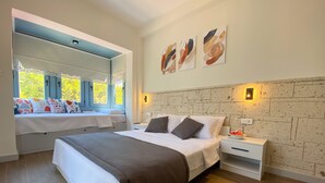 Quarto com cama grande, mesas de cabeceira, um assento à janela com almofadas e uma obra de arte na parede.