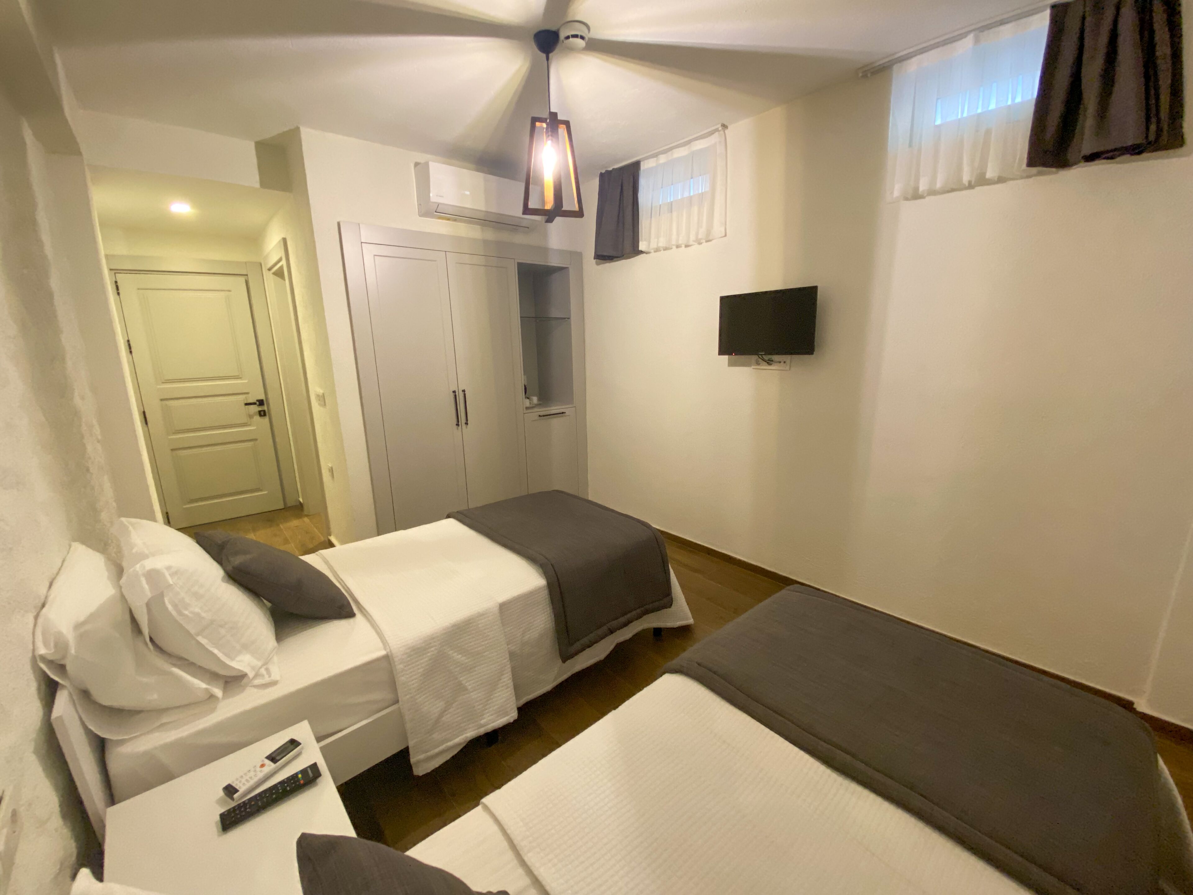 A bedroom with two beds, a wardrobe, a television, and a ceiling fan.