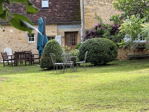 A stone building with a wooden door, a small garden with a table and chairs, and a blue umbrella. - Choubello Gite **** stars (Fajoles)