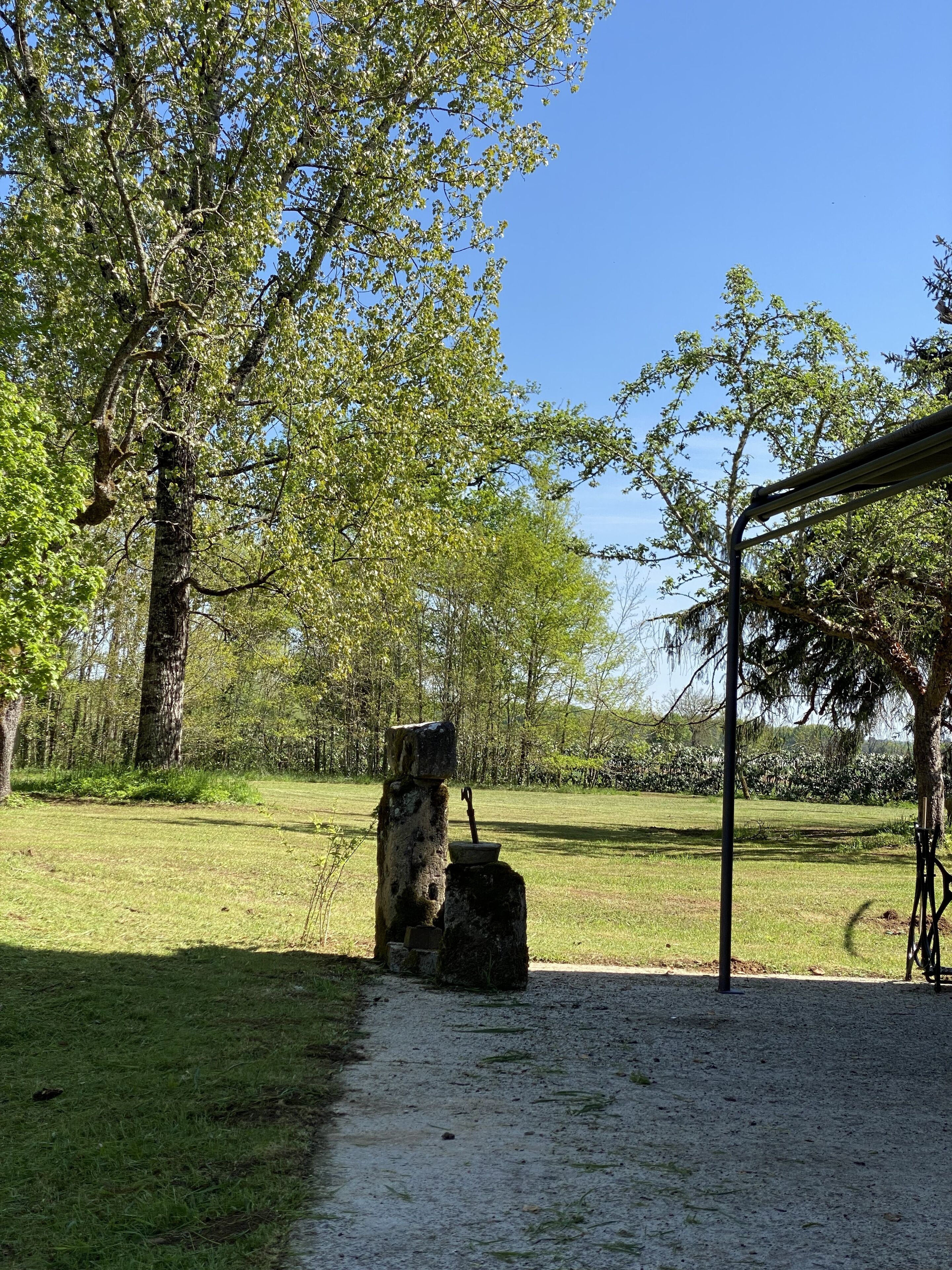 Een rustieke buitenruimte met een stenen constructie, een metalen frame en een grasveld.