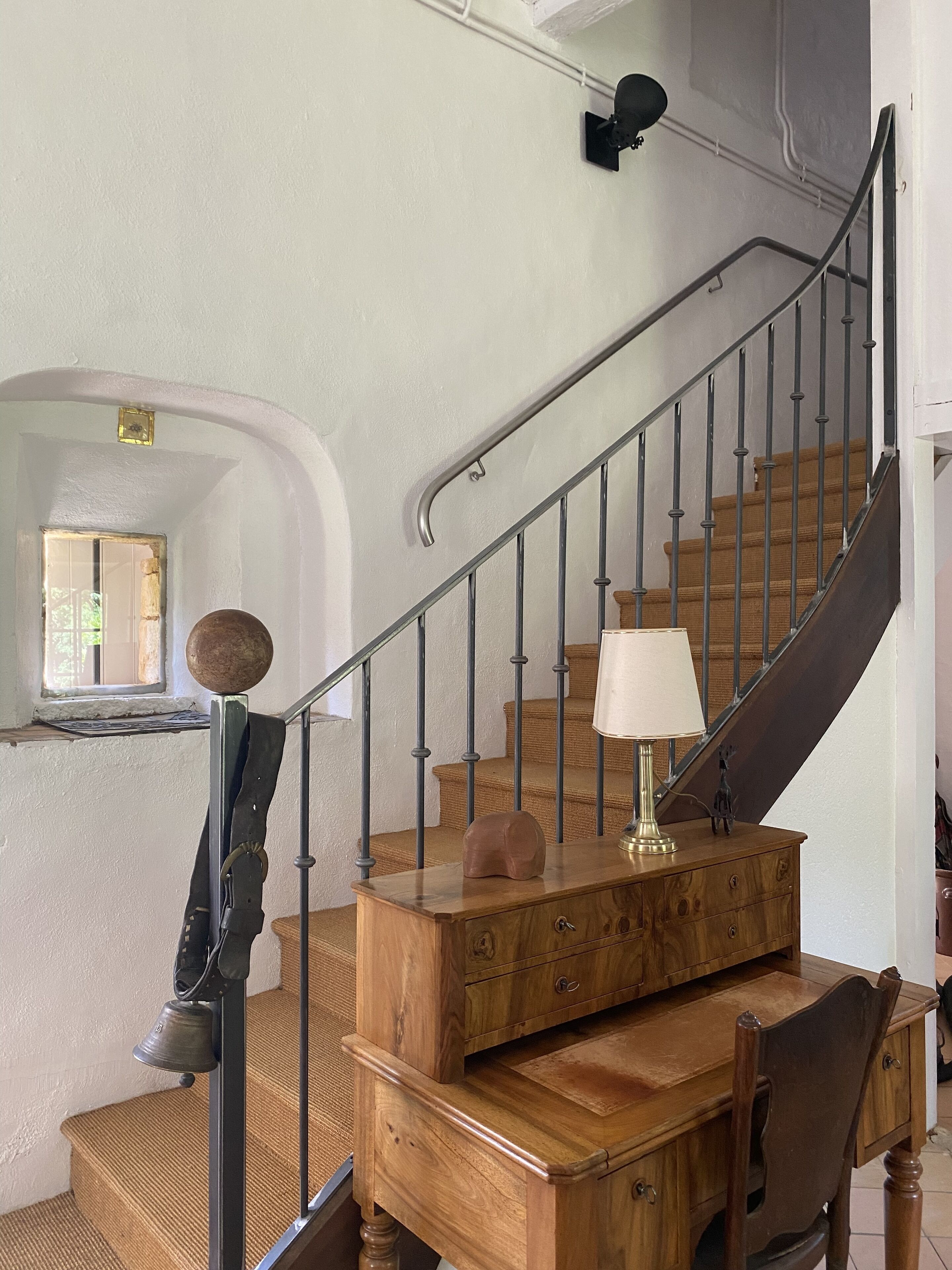 Un escalier avec une main courante en bois et des balustres en métal, une table en bois sur laquelle se trouve une lampe, et une petite statue posée sur la table.