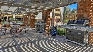 Een terras buiten met een barbecue, zithoek en een overdekte constructie met versierde zuilen.