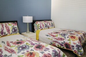 Una habitación de hotel con dos camas, cada una con ropa de cama floral, una lámpara de noche y una mesita de noche.