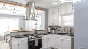 A modern kitchen with white cabinets, a stainless steel range hood, and a built-in oven. - Amazing Bungalow - by State Fair Grounds, WiFi, KG BD (Oklahoma City)
