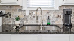 A kitchen with a granite countertop, a stainless steel sink, a coffee maker, and a window with blinds. - Amazing Bungalow - by State Fair Grounds, WiFi, KG BD (Oklahoma City)