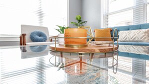 A modern living room with a glass coffee table, a blue sofa, and a large pumpkin candle. - Amazing Bungalow - by State Fair Grounds, WiFi, KG BD (Oklahoma City)