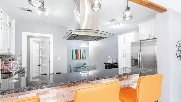 A modern kitchen with a central island, stainless steel appliances, and orange bar stools. - Amazing Bungalow - by State Fair Grounds, WiFi, KG BD (Oklahoma City)