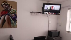 Une pièce comprenant un bureau, une chaise, un téléviseur fixé au mur et une petite étagère.