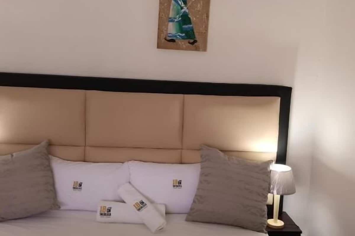 A hotel room with a large bed, beige headboard, and a painting above it.