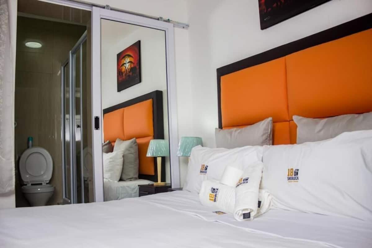 A hotel room with a bed, a nightstand, a lamp, and a bathroom visible through an open door.