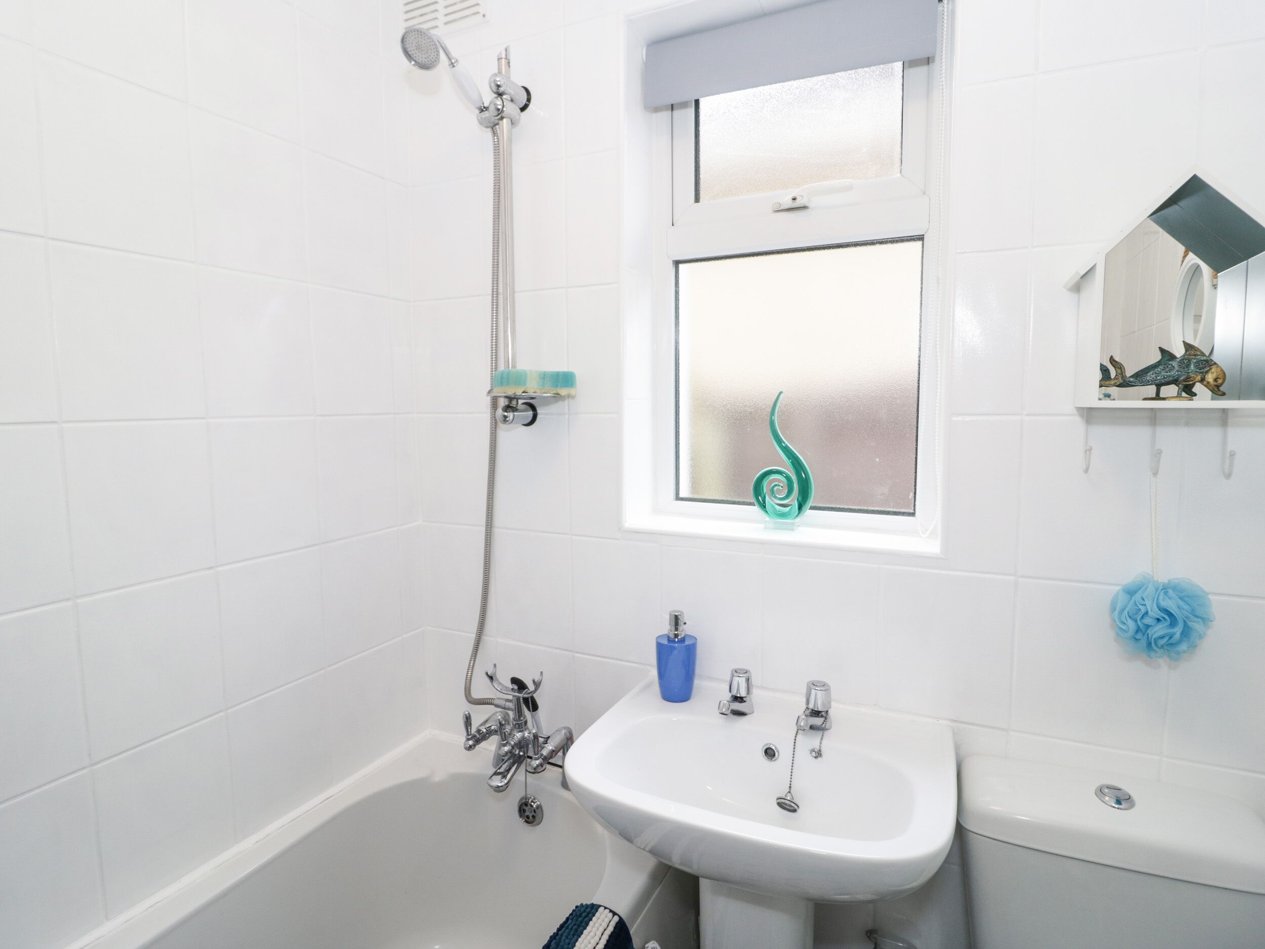A bathroom with a bathtub, a sink, a toilet, a showerhead, a window, and a decorative fish sculpture.