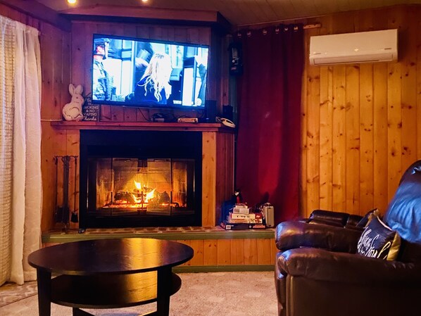 Una sala de estar acogedora con chimenea, televisor montado encima y un sofá de cuero.
