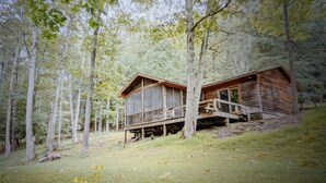 A cabin with a deck and a covered area, surrounded by tall trees.