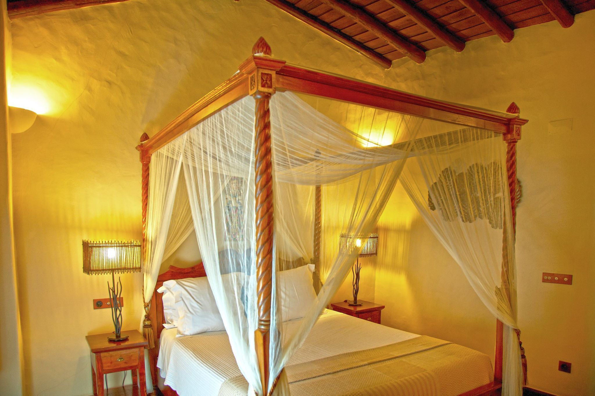 A four-poster bed with a canopy, bedside lamps, and a small table with a decorative item.