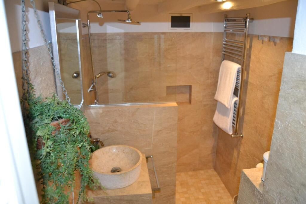 Une petite salle de bain fermée, dotée d’une douche en verre, d’un lavabo rond et d’un porte-serviettes.