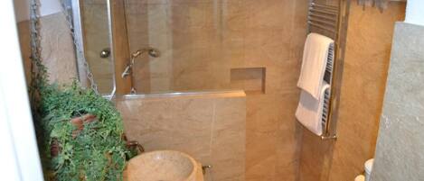 A small, enclosed bathroom with a glass shower enclosure, a round sink, and a towel rack.