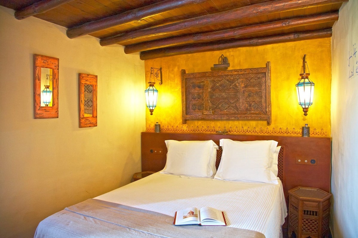 A neatly made bed with a book on it, two wall-mounted lamps, and a decorative wooden headboard.