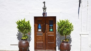 A double wooden door with a sign above it, flanked by two large potted plants. - Casa pinto (Reguengos de Monsaraz)