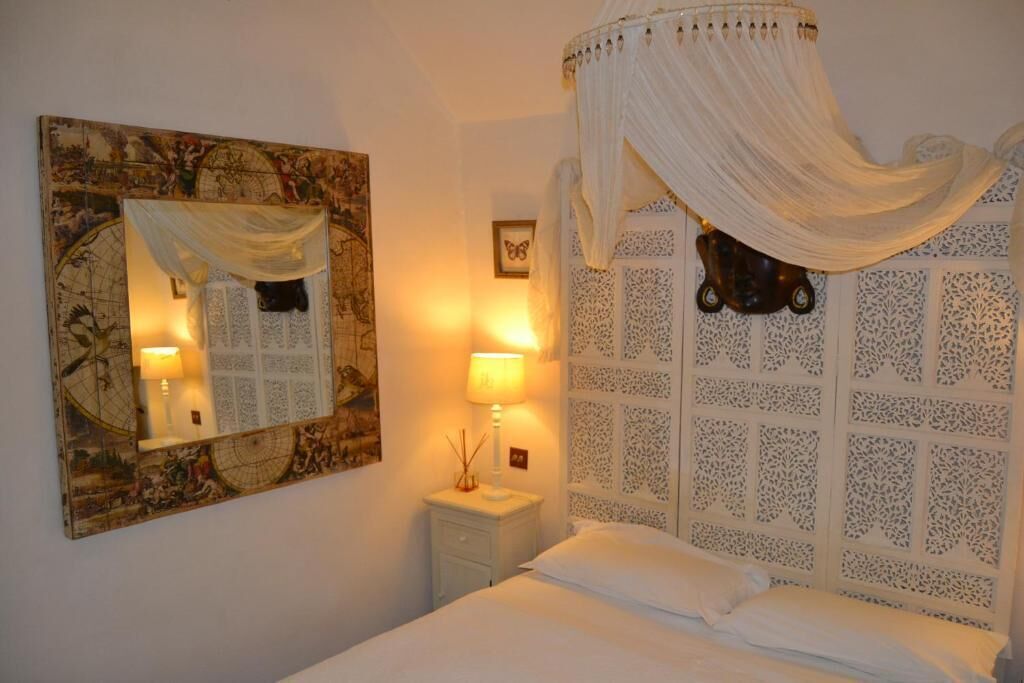 Une chambre à coucher avec un lit à baldaquin, une table de chevet avec une lampe, un miroir et un panneau décoratif mural.