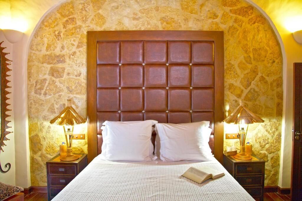 A bedroom with a large bed, two bedside tables with lamps, and a stone wall.