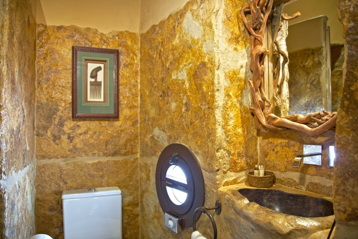 A stone bathroom with a toilet, a sink, and a mirror.