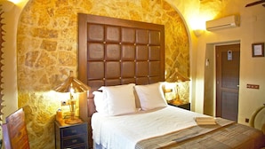 A bedroom with a stone wall, a wooden headboard, two bedside tables with lamps, and a door with a sign. - Casa pinto (Reguengos de Monsaraz)