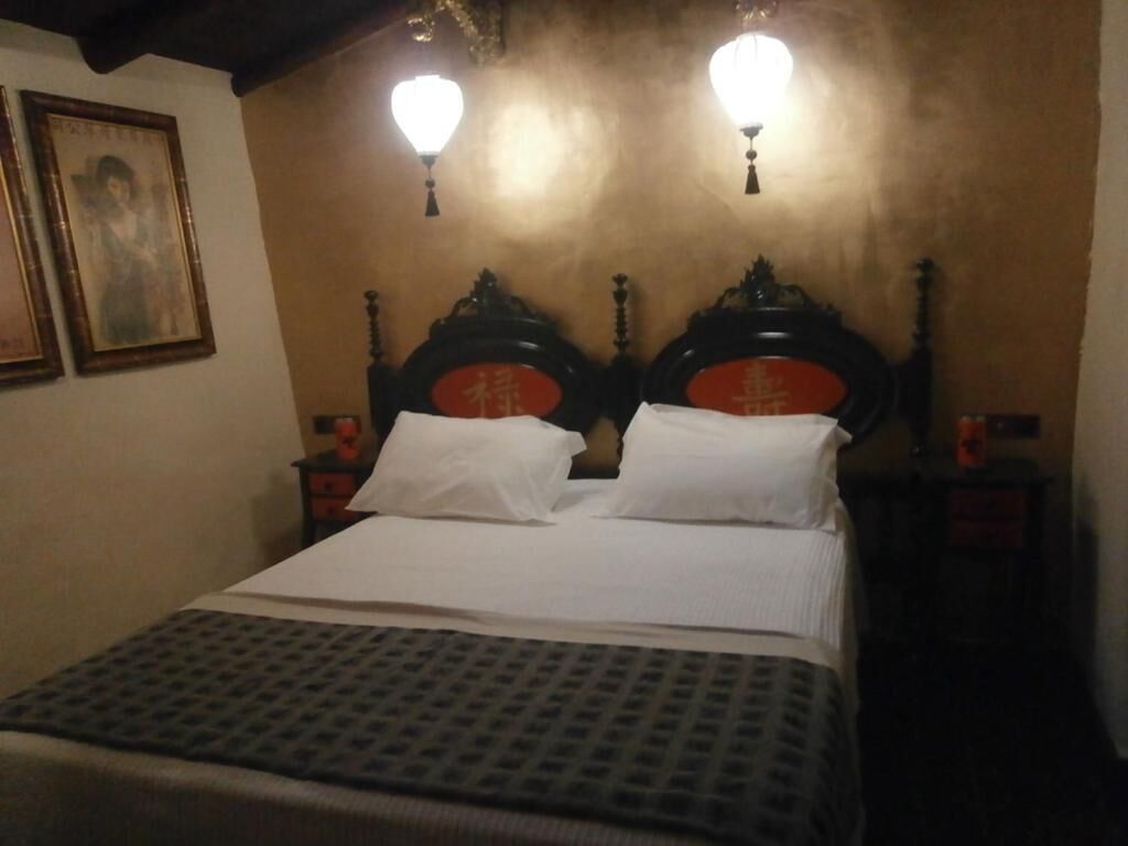 A neatly made bed with a patterned bedspread, two wall-mounted lamps, and a framed picture on the wall.