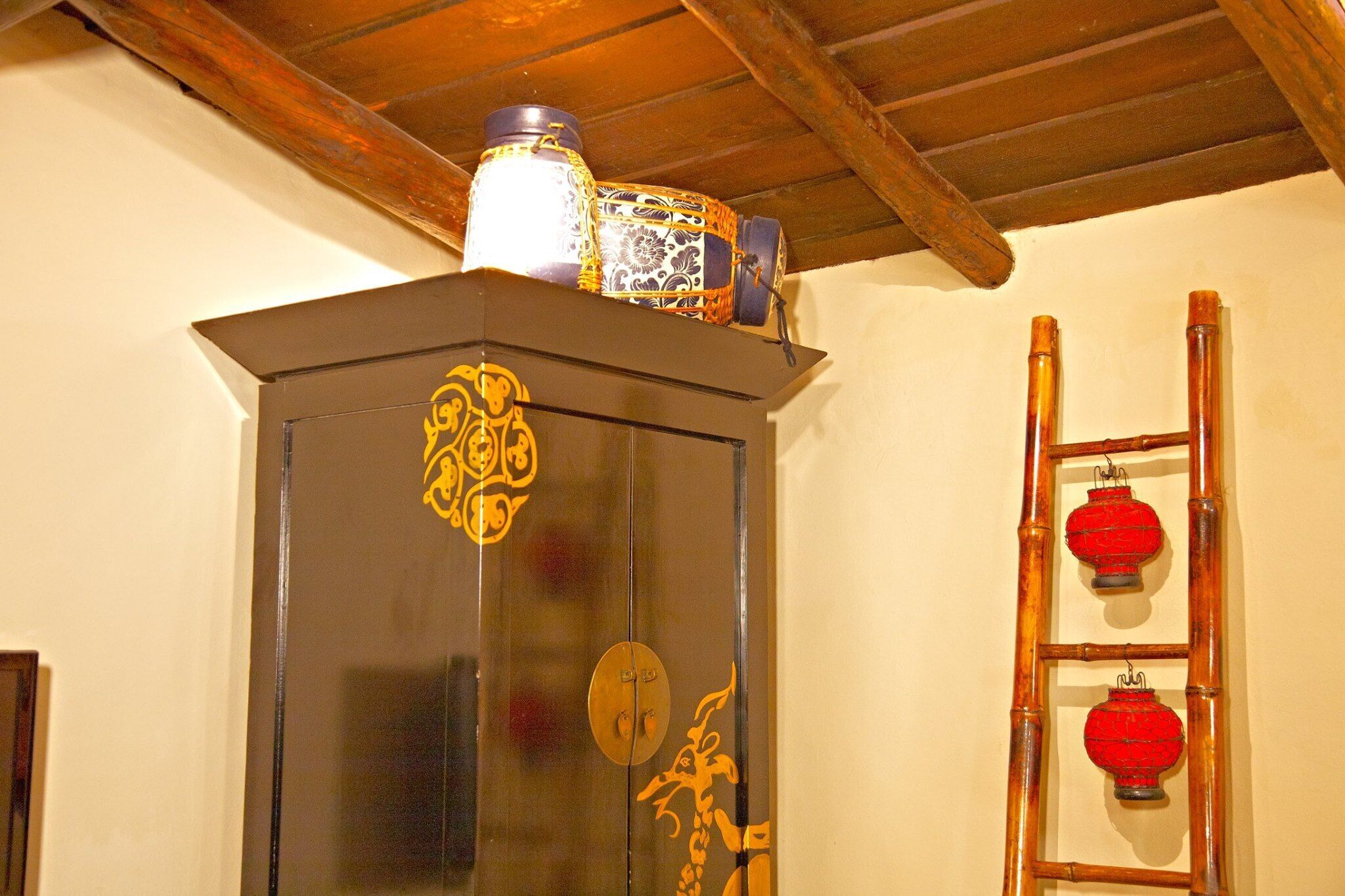 Ein traditioneller chinesischer Schrank mit aufwendigen Verzierungen, eine Holzleiter mit roten Laternen und ein dekorativer Behälter obenauf.