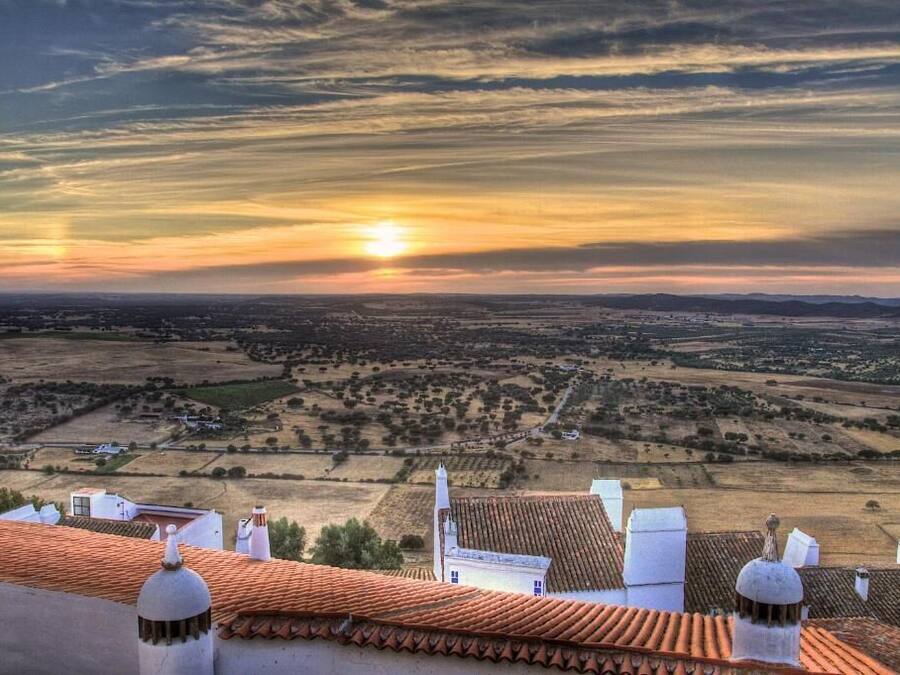 Vista panorâmica de uma paisagem rural com campos em socalcos e um pôr do sol.