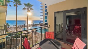 A balcony with a view of the ocean, a pool, and a dining area with red chairs.