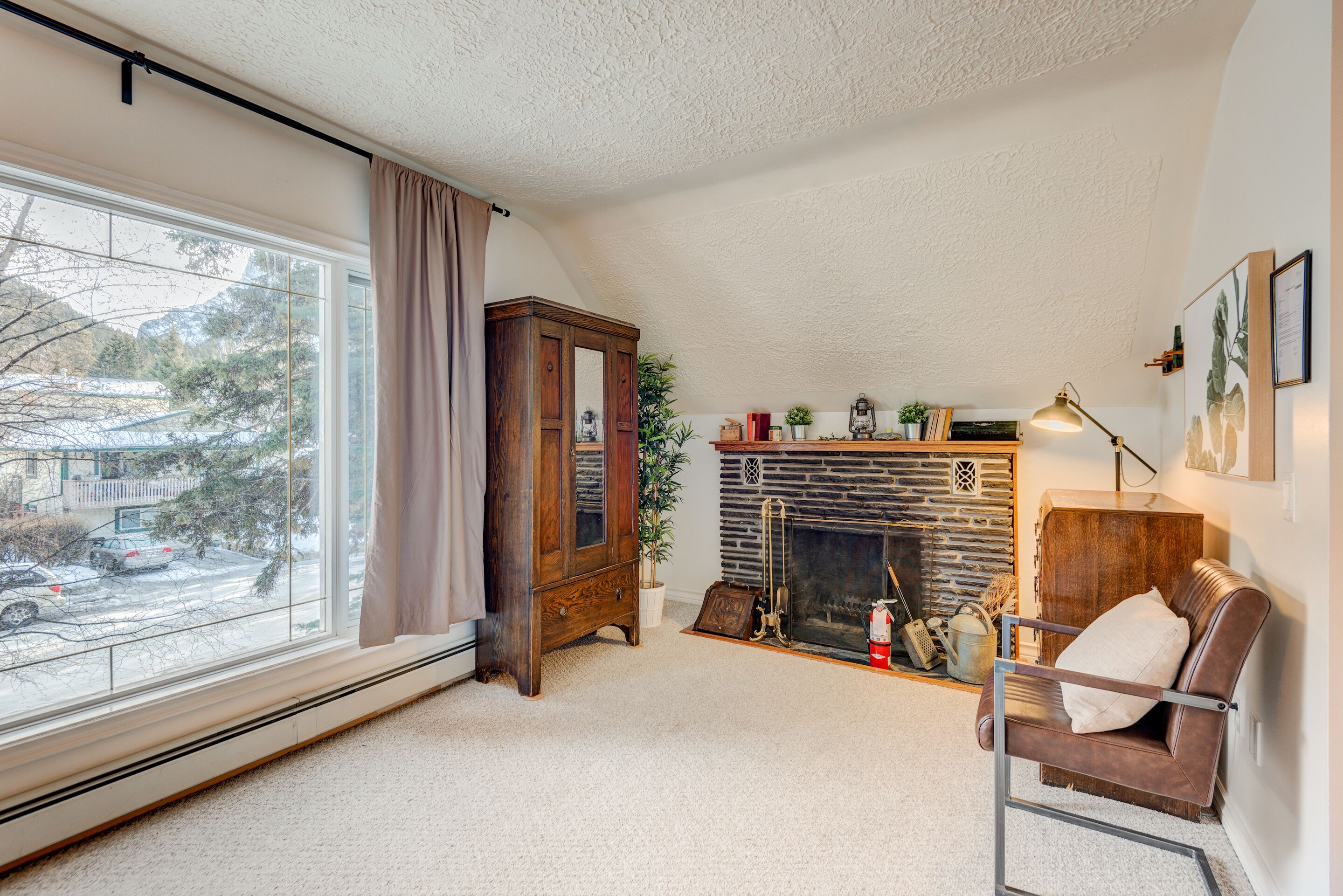 A cozy living room with a fireplace, a large window with curtains, and a leather armchair.