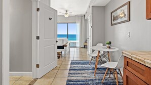 A hotel room with a bed, a dining table with chairs, a ceiling fan, and a view of the ocean. - Origin 0538- Studio - Breath Taking Gulf Views (Panama City Beach)