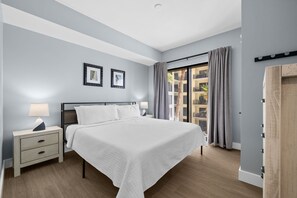 Quarto com cama, mesas de cabeceira, abajur, moldura de quadro, cortina e vista para o exterior.