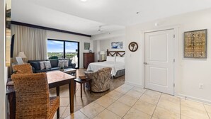 Une chambre d’hôtel avec un lit, un canapé, une table à manger et une chaise. Il y a une fenêtre avec vue, une porte et un mur sur lequel est affiché un panneau.