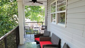 A covered porch with wicker furniture and a glass table, overlooking a street with parked cars and greenery. - Walk to Stadium/Strip/Downtown! 2 bd/2 bath, Off-street parking! (Tuscaloosa)