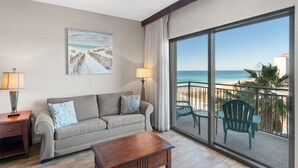 Ein Balkon mit Blick auf den Strand und den Ozean, eine Couch, ein Tisch und zwei Stühle.