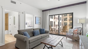 A modern living room with a grey sofa, wooden coffee table, and a view of a balcony with outdoor furniture. - Origin 0708 - One Bedroom -Pool and Gulf Views (Panama City Beach)