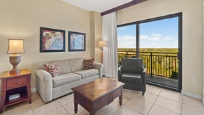 A living room with a sofa, a coffee table, a chair, and a large window with a balcony. - Origin 0715 - Studio King - Quiet Nature View Unit (Panama City Beach)