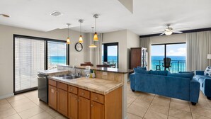 A modern kitchen with a central island, a dining area with a view, and a living room with a blue sofa.