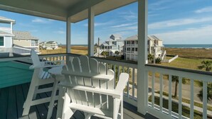 Une véranda couverte, avec des fauteuils Adirondack blancs, donnant sur les maisons du bord de mer.