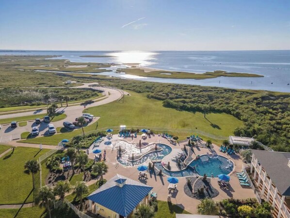 An aerial view of a resort with a large pool area, multiple swimming pools, and a view of the ocean.