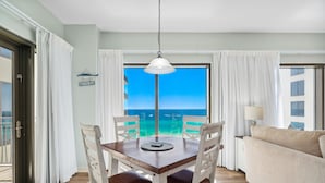 Un coin repas comprenant une table et des chaises, un luminaire suspendu et une vue sur l’océan par une grande fenêtre.