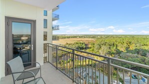 Ein Balkon mit Glastür, einem Stuhl und Blick auf eine grüne Landschaft.