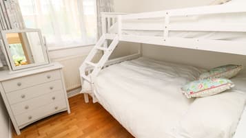 A bunk bed with white bedding, a dresser with drawers, a mirror, and two decorative pillows.