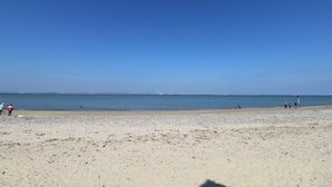 Una playa con cielo despejado, mar tranquilo y edificios a lo lejos.