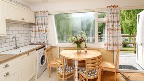 Una cocina con lavadora, lavabo, ventana con cortinas y una mesa con sillas.