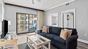 Ein modernes Wohnzimmer mit einem dunkelblauen Sofa, einem Glastisch und einem Deckenventilator.